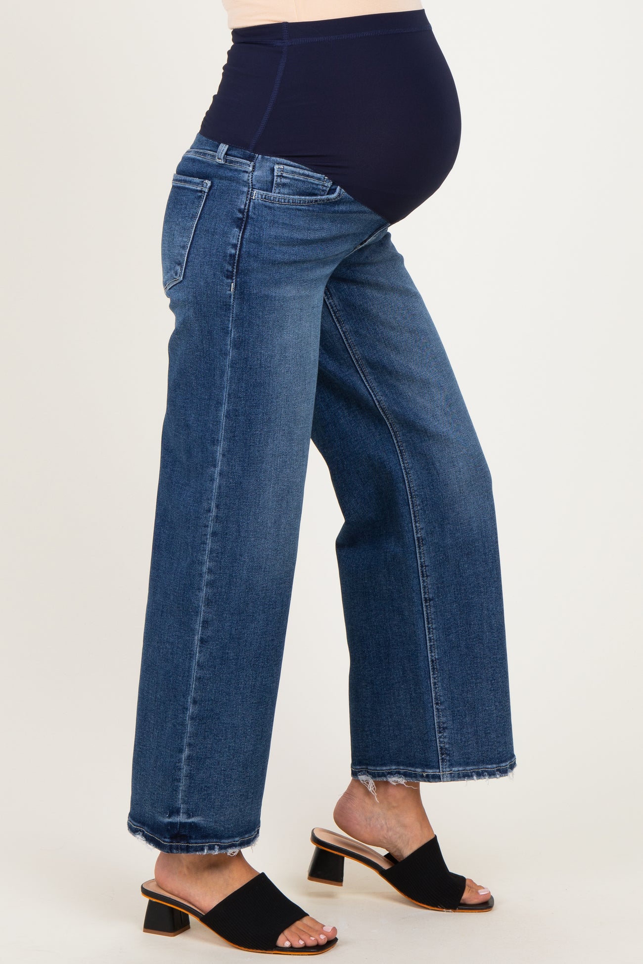 woman wearing a pair of dark blue maternity jeans with a stretchy waistband and frayed hem, showing a baby bump