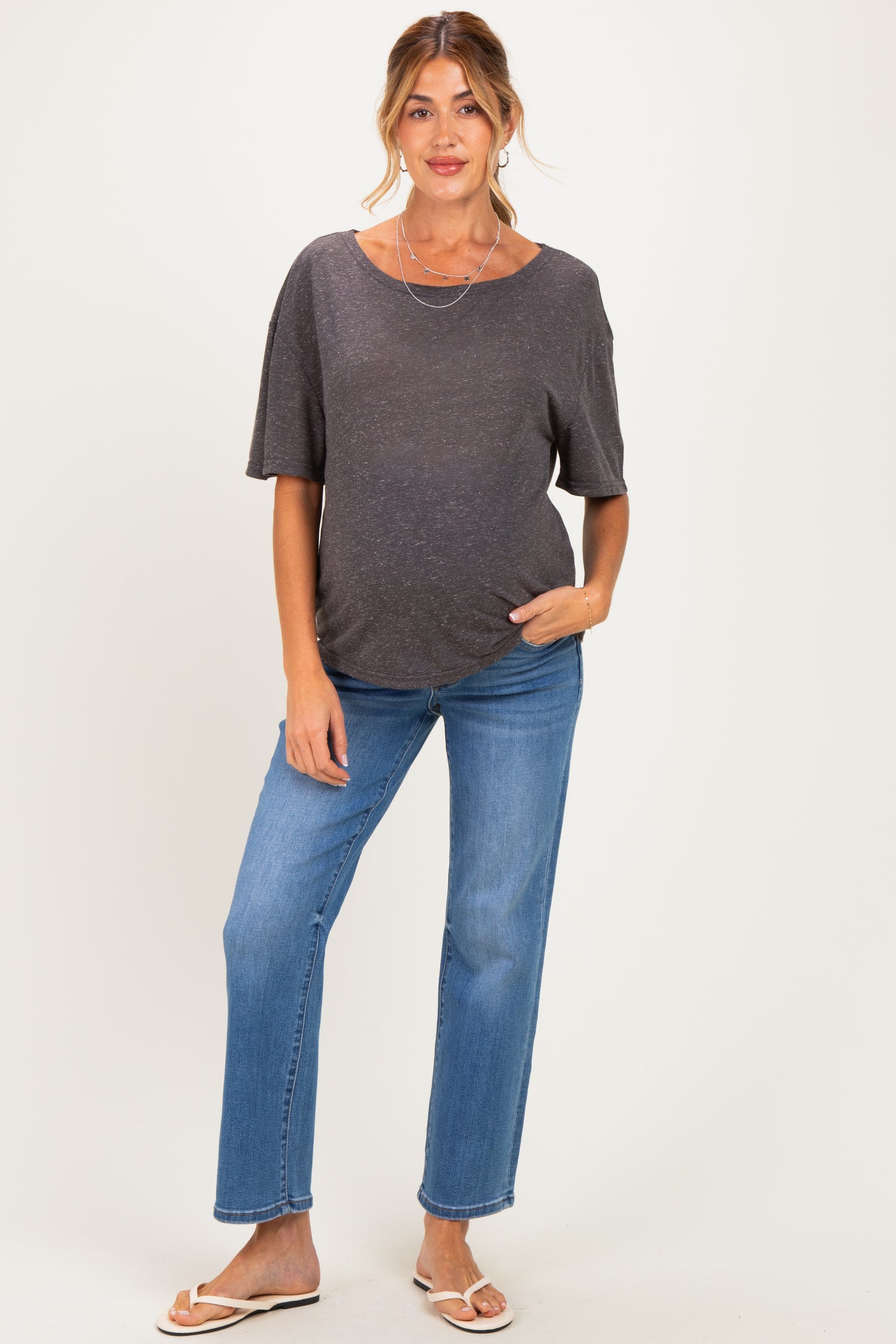 woman wearing a dark gray short sleeve maternity top and blue straight leg maternity jeans, showing her baby bump