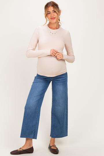 woman wearing a light beige long sleeve maternity top and wide-leg blue maternity jeans with a visible baby bump