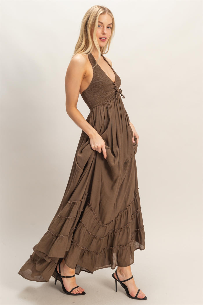 woman wearing a brown halter neck maxi dress with ruffles and a smocked bodice, standing sideways