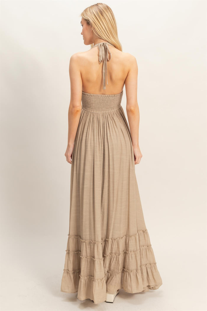 woman wearing a light brown halter-style maxi dress with a smocked bodice and tiered ruffle hem