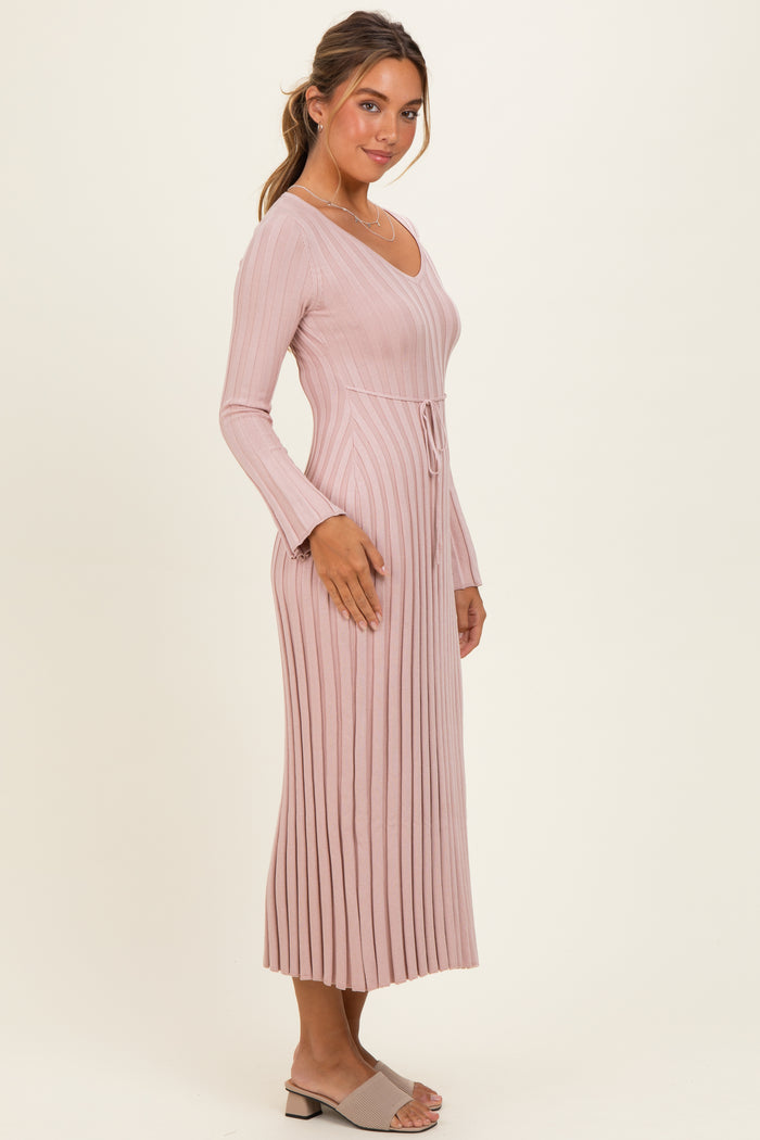 woman wearing a long sleeve ribbed pink dress with a drawstring waist and side slits, standing against a neutral background