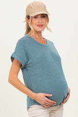 woman wearing a teal maternity top with rolled sleeves and holding her baby bump