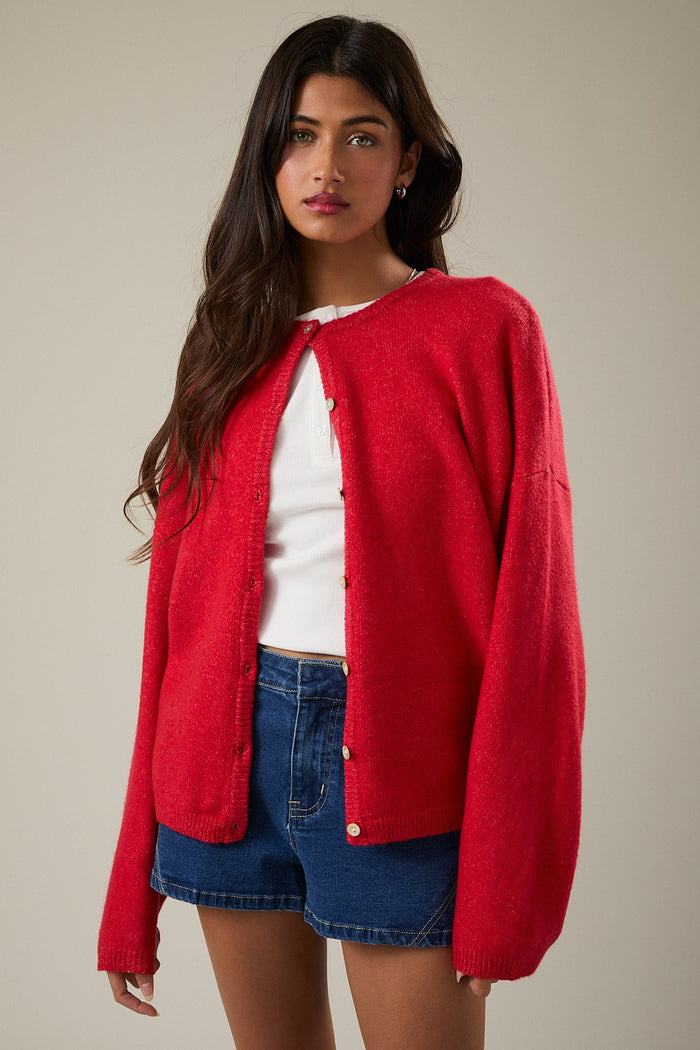 woman wearing a red oversized cardigan over a white top and blue denim shorts