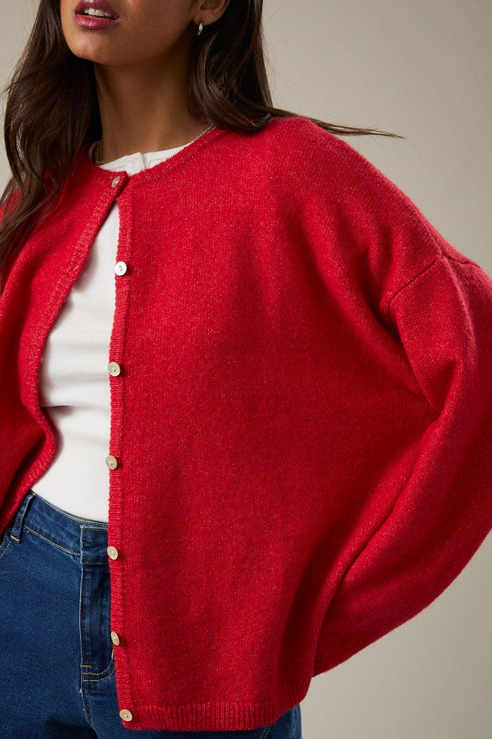 woman wearing a bright red oversized cardigan with buttons over a white top and blue jeans