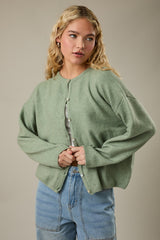 woman wearing a light green oversized cardigan with button closure, paired with a white ribbed top and high-waisted jeans