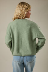 woman wearing a light green oversized sweater with long sleeves and back-facing view paired with light blue jeans