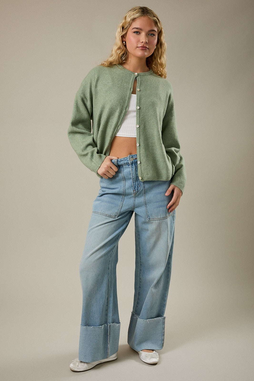 woman wearing a green cardigan over a white crop top and light blue wide-leg jeans