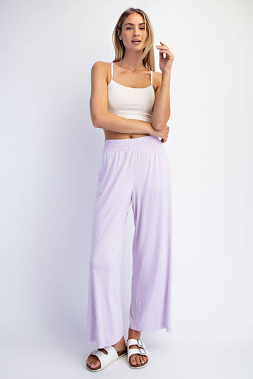 woman wearing a light purple wide leg pants and a white crop top, posing with arms crossed