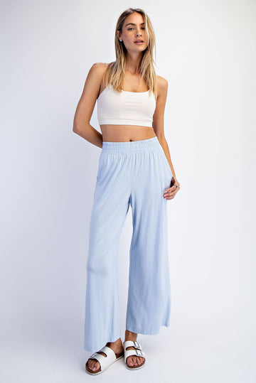 woman wearing a light blue wide-leg pants and a white crop top, standing with one hand on her hip