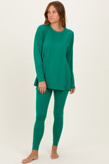 woman wearing a green long sleeve top and matching leggings, standing barefoot against a neutral background
