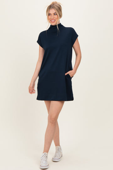 woman wearing a navy blue short sleeve mock neck dress with side pockets and white sneakers