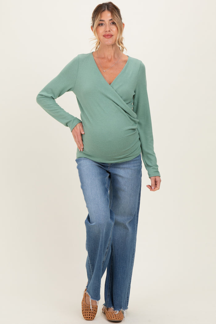 woman wearing a green long sleeve wrap maternity top and blue jeans, showing her baby bump