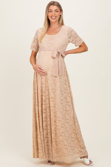 woman wearing a beige lace maternity maxi dress with a tied waist and holding her baby bump