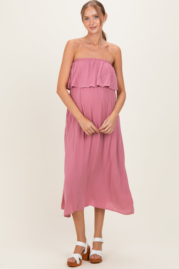 woman wearing a pink strapless maternity dress with a ruffled bodice and a flowing skirt, holding her baby bump