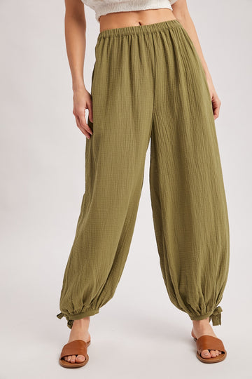 woman wearing olive green wide-leg pants with a textured finish and gathered cuffs, styled with brown sandals