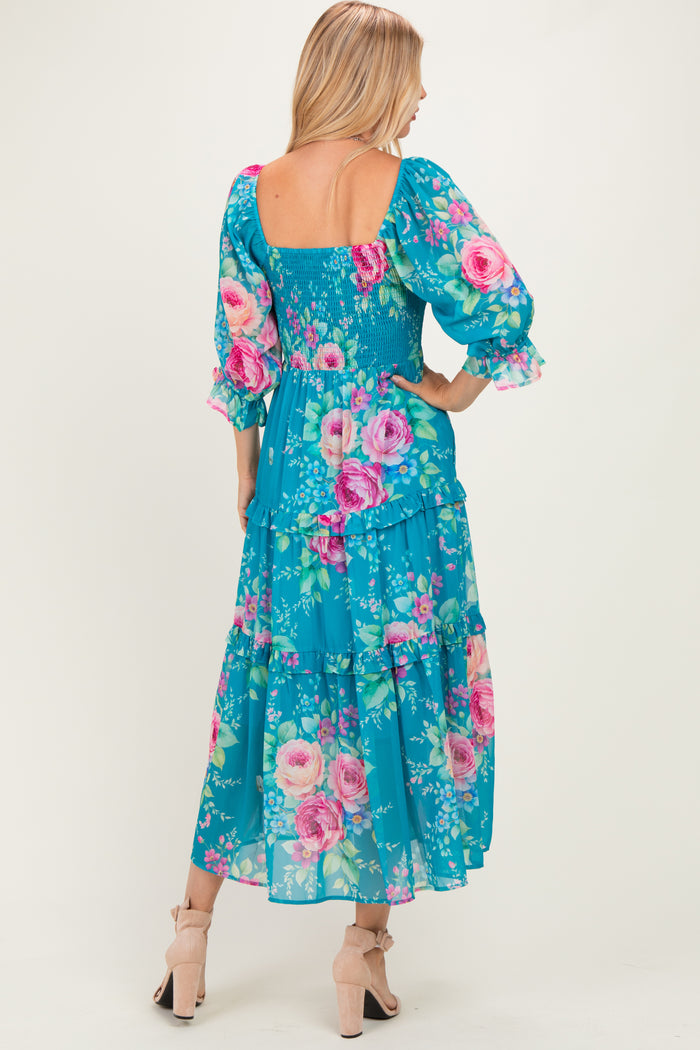 woman wearing a blue floral maxi dress with puff sleeves and a smocked bodice, showing a tiered design and back view
