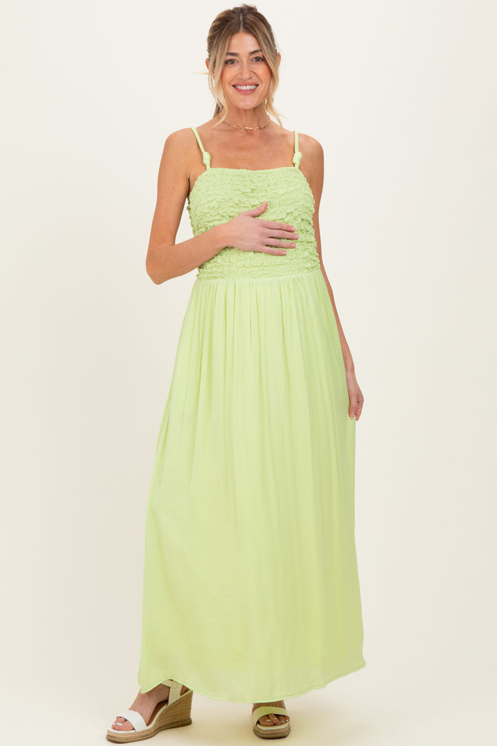 woman wearing a light green maternity maxi dress with smocked bodice and holding her baby bump