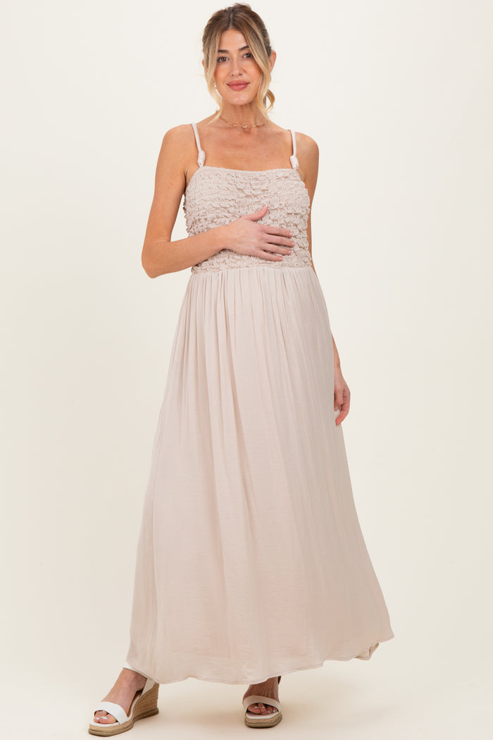 woman wearing a light beige maternity maxi dress with a smocked bodice, holding her baby bump