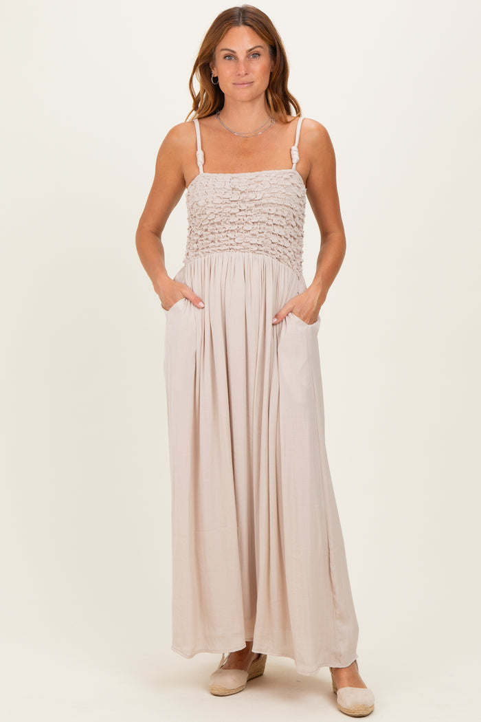woman wearing a beige maxi dress with smocked bodice and pockets, standing on a neutral background
