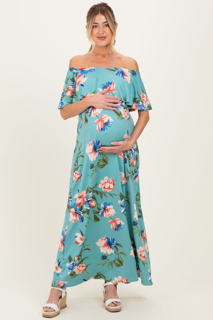 woman wearing a floral off-the-shoulder maternity maxi dress and cradling her baby bump