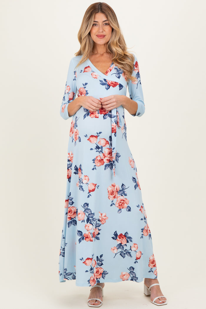 woman wearing a light blue floral maternity maxi dress with three-quarter sleeves and a v-neckline, holding her baby bump
