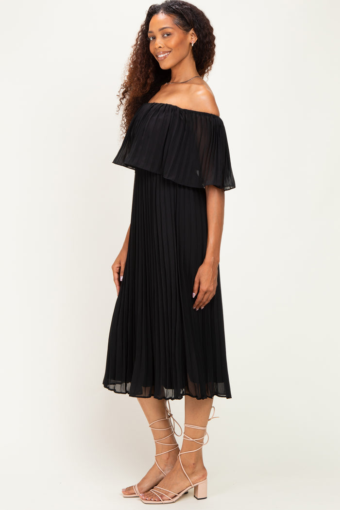 woman wearing a black off-the-shoulder pleated midi dress with a flowy silhouette and matching sandals