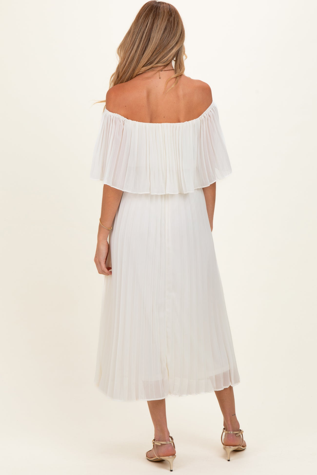 woman wearing a white off-the-shoulder maternity dress with a flowy pleated design and knee-length hem