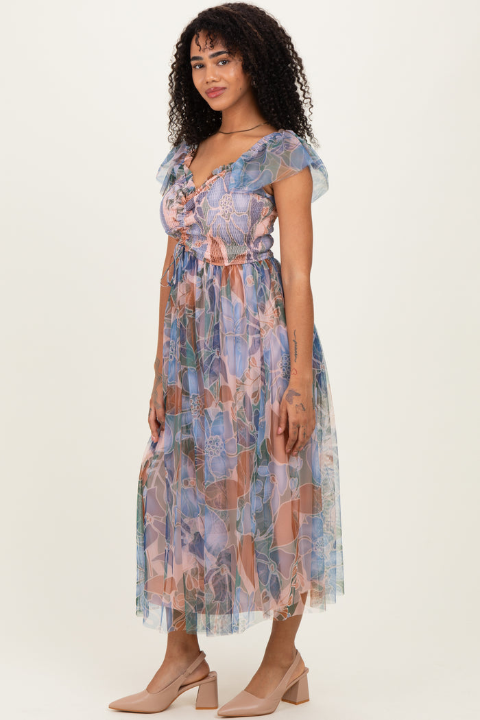 woman wearing a patterned pastel maxi dress with short ruffled sleeves and a cinched waist, styled with nude heels