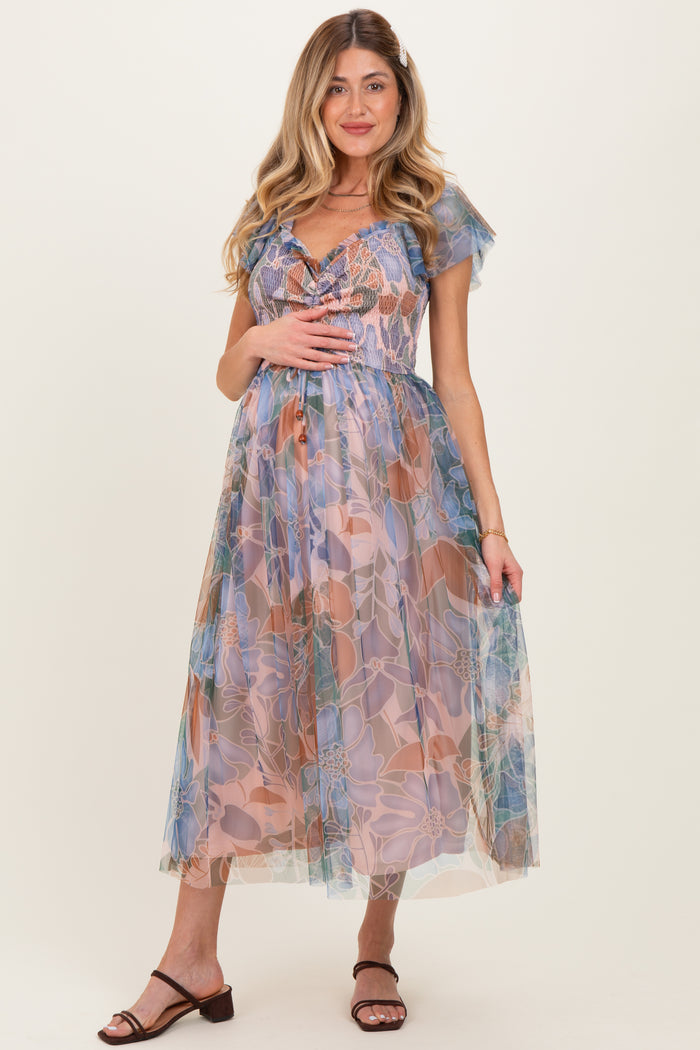 woman wearing a floral maternity dress with a sheer overlay and a baby bump visible