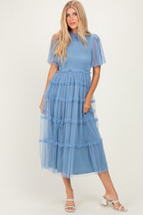 woman wearing a light blue tiered midi dress with puff sleeves and ruffled details, styled with white heels