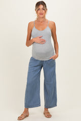 woman wearing a gray maternity tank top and blue wide-leg pants, gently holding her baby bump