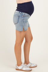 woman wearing a navy blue maternity top and distressed denim maternity shorts with a visible baby bump