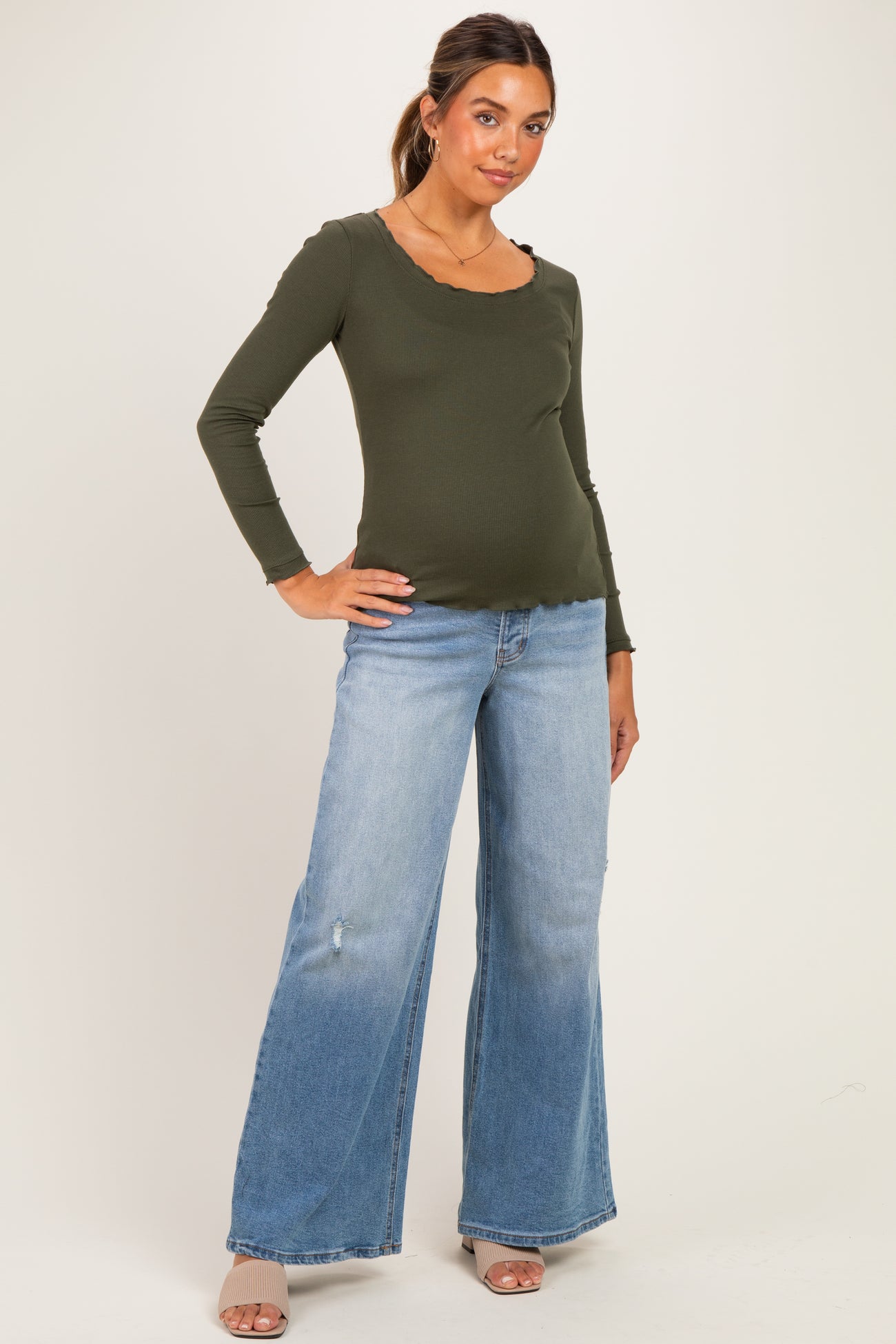 woman wearing an olive green long sleeve maternity top and light wash wide-leg jeans, showing her baby bump