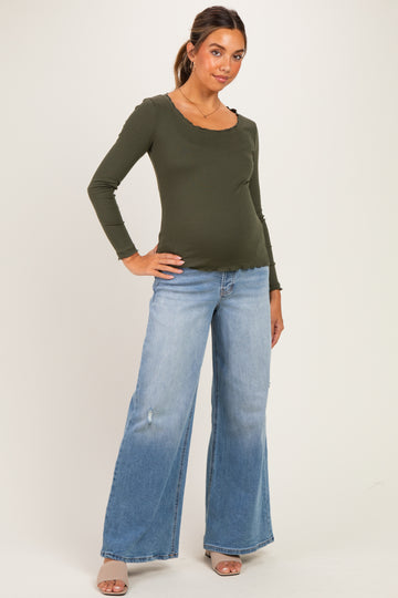 woman wearing an olive green long sleeve maternity top and light wash wide-leg jeans, showing her baby bump