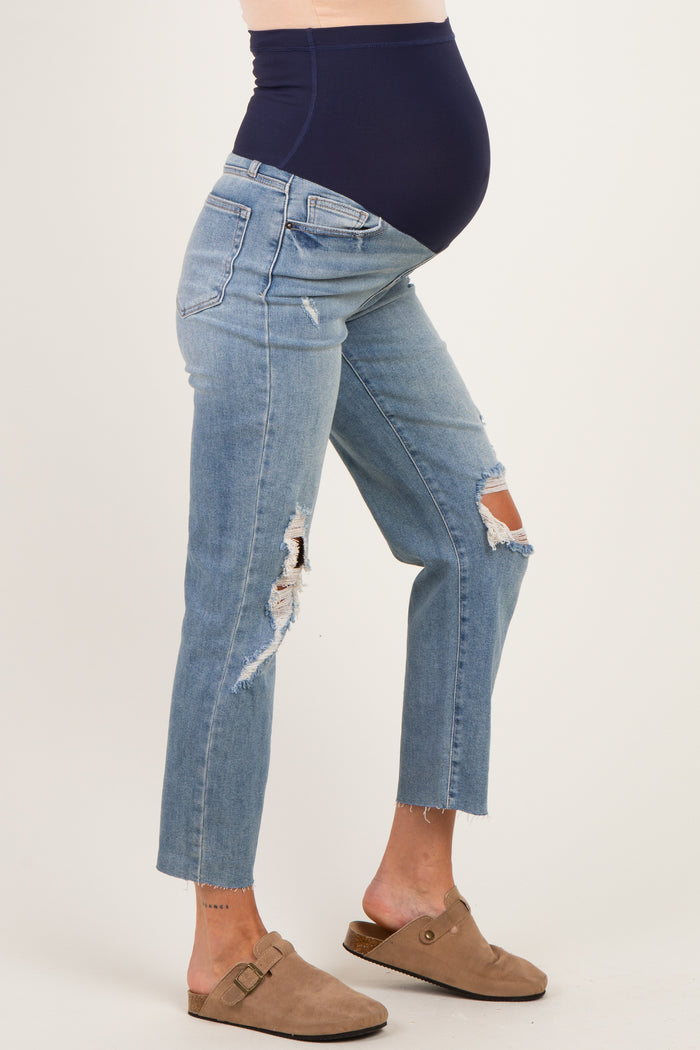 woman wearing distressed light blue maternity jeans with a navy blue over-the-belly panel and a visible baby bump