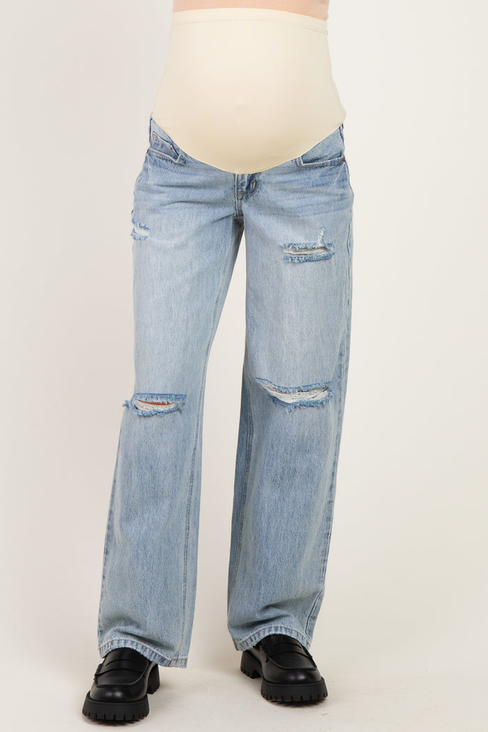 woman wearing distressed light blue maternity jeans with a beige over-the-bump waistband and a visible baby bump