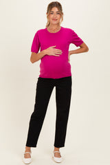 woman wearing a bright pink maternity top and black pants, holding her baby bump