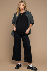 woman wearing a black maternity top, gray checkered shirt, and black wide-leg pants, showcasing her baby bump