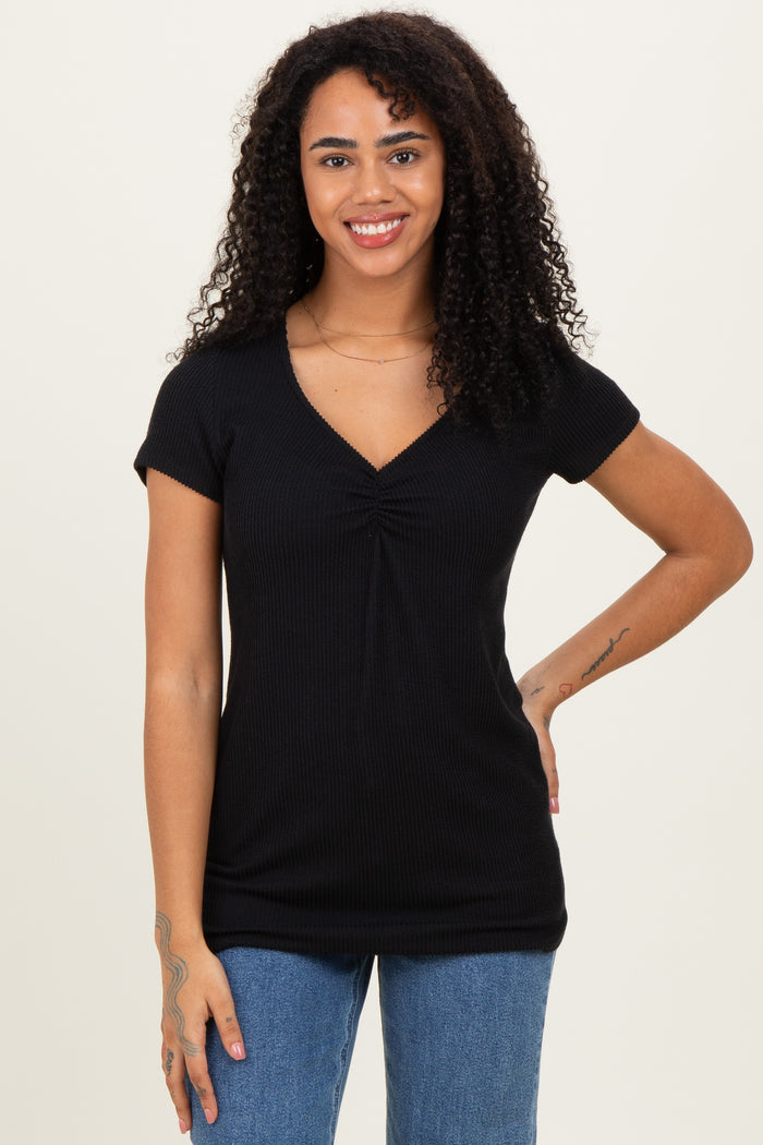 woman wearing a black short sleeve top with a ruched v-neck and standing with one hand on her hip