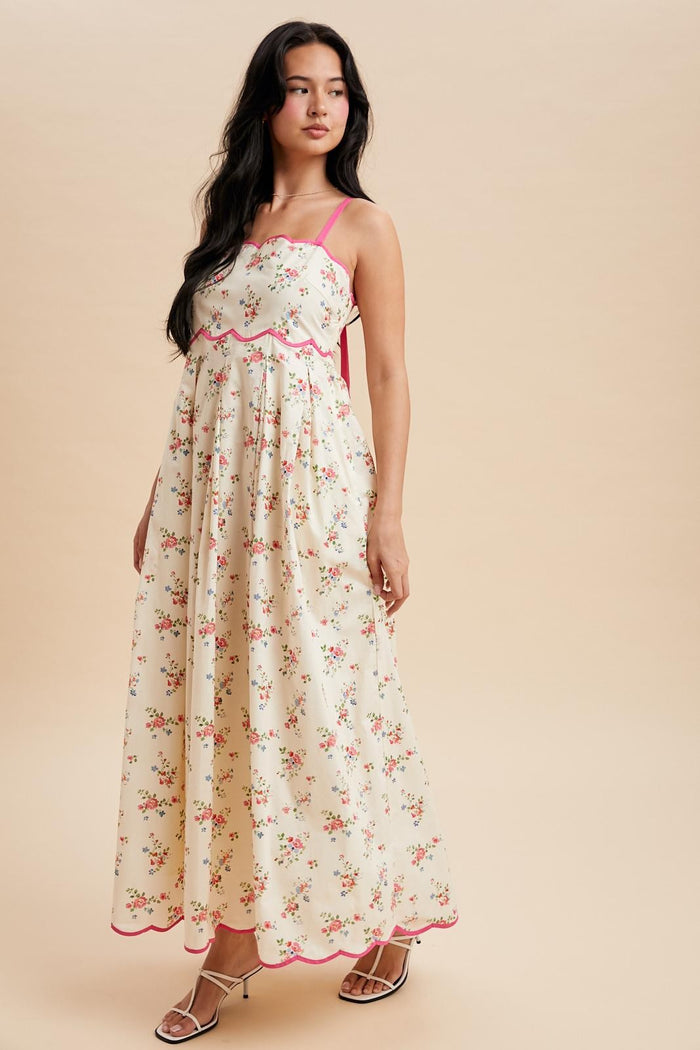 woman wearing a cream floral maxi dress with scalloped hem and pink trim, standing against a neutral background