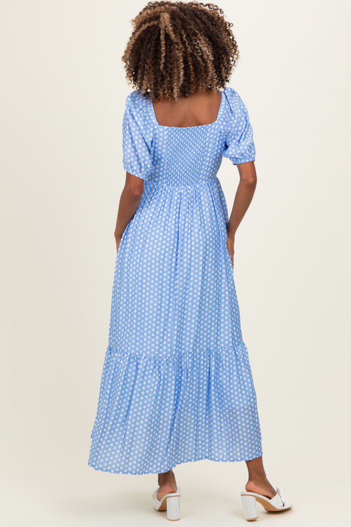 woman wearing a blue polka dot maternity maxi dress with puff sleeves and a tiered skirt, showing her baby bump from the back