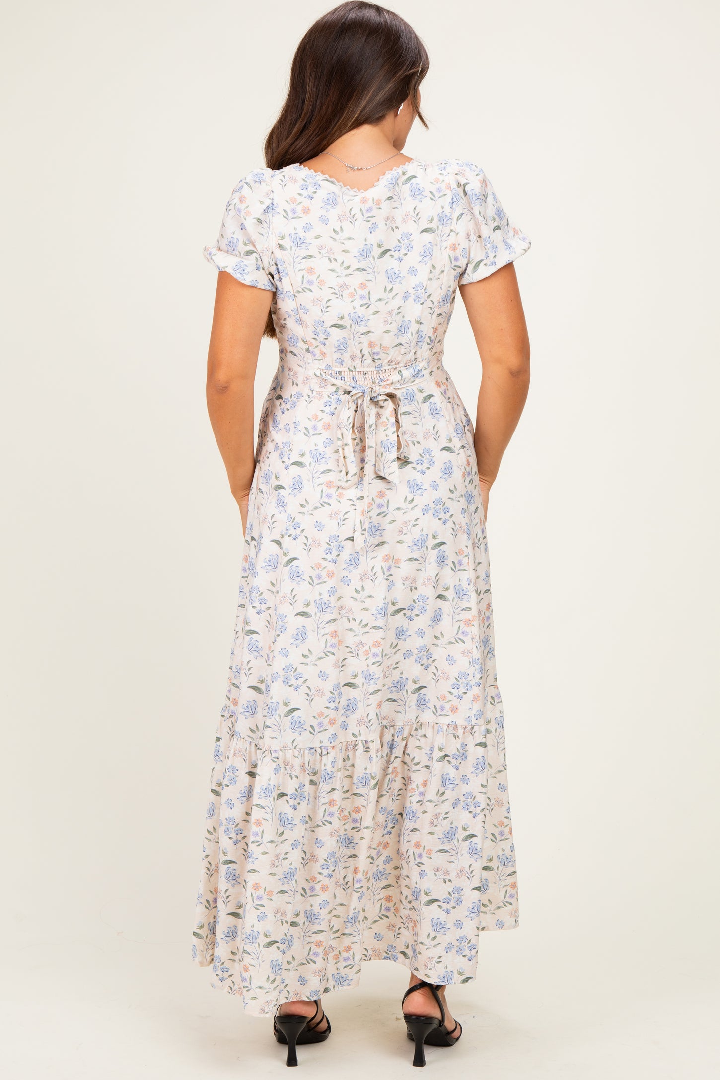 woman wearing a back view of a floral print maternity maxi dress with short sleeves and a tiered skirt