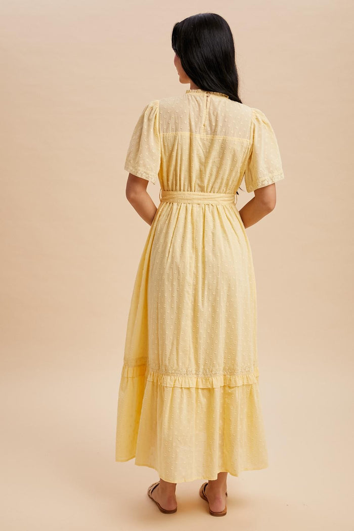 woman wearing a yellow short sleeve maxi dress with a tie waist and ruffle hem, shown from the back