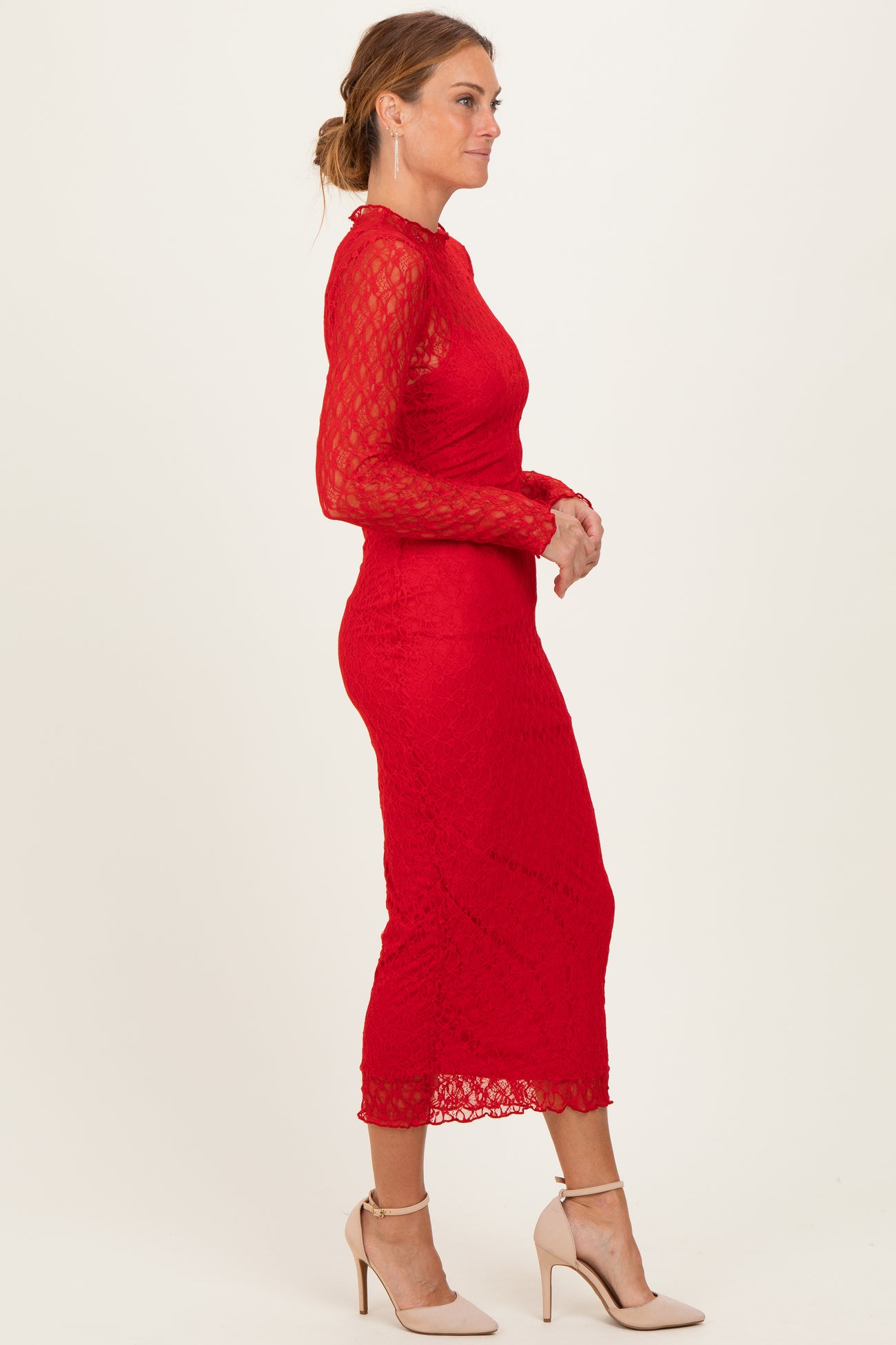 woman wearing a long sleeve red lace midi dress and nude high heels, standing in profile