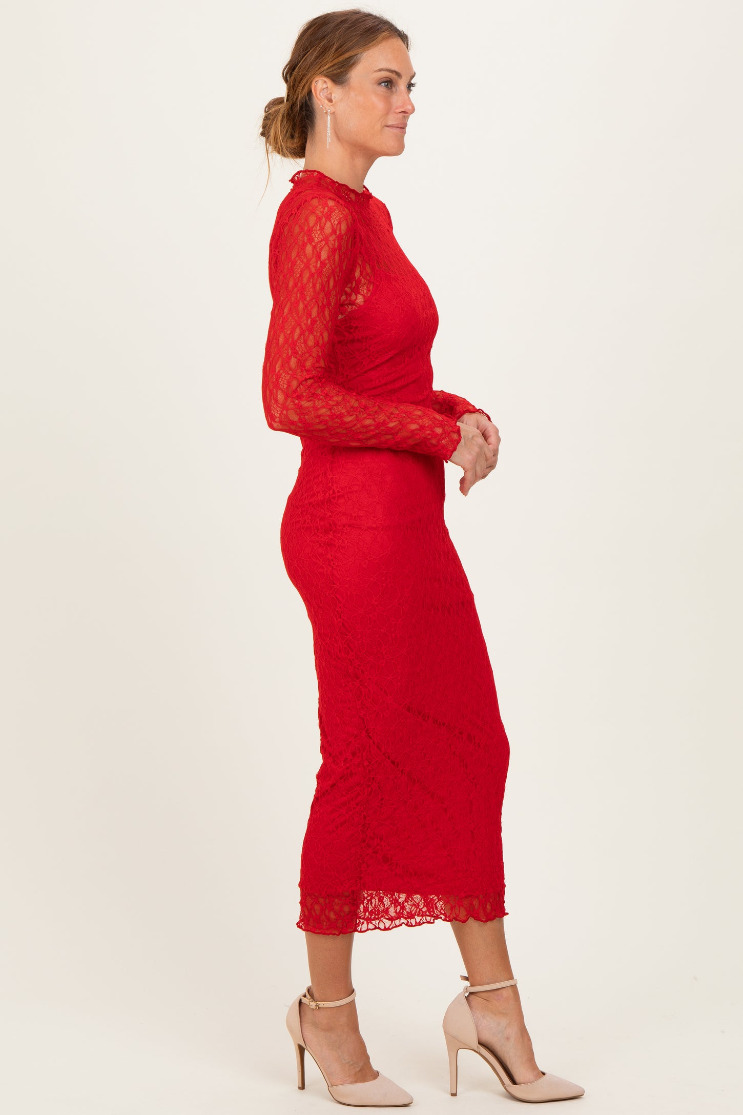 woman wearing a long sleeve red lace midi dress and nude high heels, standing in profile
