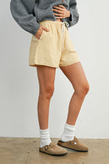 woman wearing yellow striped drawstring shorts with a grey sweater and brown clogs, standing with one hand on her hip