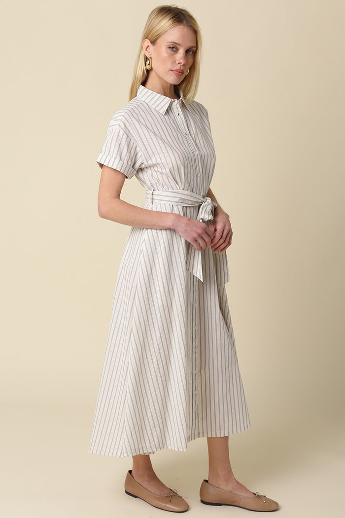 woman wearing a beige striped button-up dress with a tied waist and short sleeves, standing against a neutral background