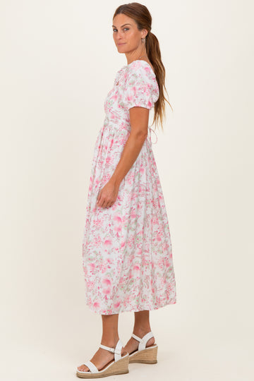woman wearing a floral pink midi dress with short puff sleeves and a fitted waist, styled with white wedge sandals