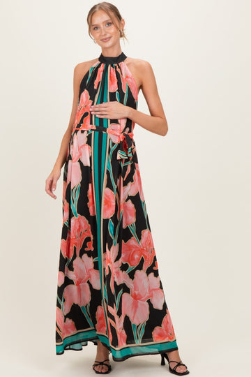 woman wearing a black floral maxi maternity dress with a halter neck and a tied waist, holding her baby bump